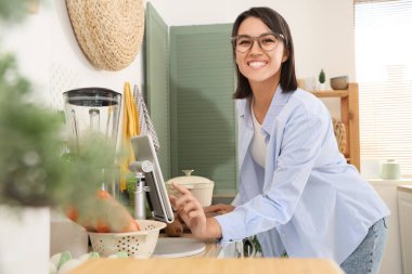 Mutfakta tablet bilgisayar kullanan blenderi olan genç bir kadın.