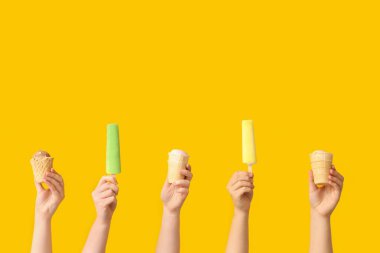 Sarı arka planda farklı tatlı dondurmalı kadın elleri.