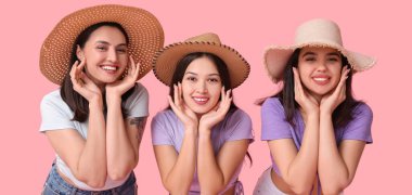 Pembe arka planda plaj şapkalı güzel genç kadınlar.