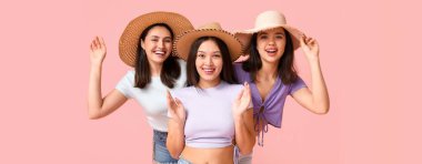 Pembe arka planda plaj şapkalı güzel genç kadınlar.