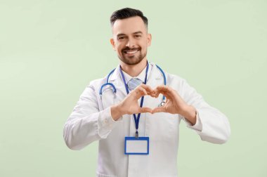 Erkek doktor yeşil arka planda elleriyle kalp yapıyor.