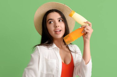 Yeşil arka planda güneş kremi şişeleri olan güzel genç bir kadın.