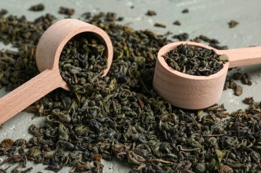 Ahşap kaşıklar, kuru yeşil çay yaprakları ve grunge yeşil arka plan.