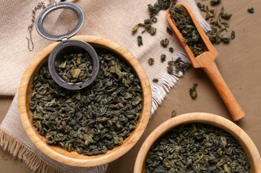 Kepçeli ahşap kaseler ve kahverengi arka planda kuru yeşil çay yaprakları.