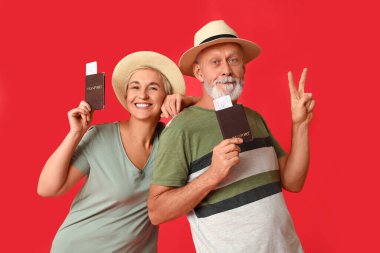 Kırmızı arka planda pasaportları olan olgun bir çift. Seyahat kavramı