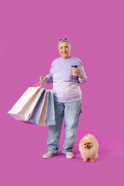 Alışveriş torbaları ve mor arka planda Pomeranya köpeği olan yaşlı bir kadın.