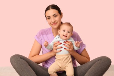 Küçük bebeğiyle pembe duvarın yanında yoga yapan güzel, genç ve sportif bir kadın.