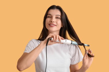 Güzel, genç, mutlu bir kadın sarı arka planda saçlarını kıvırıyor.