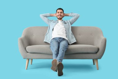 Yakışıklı genç adam, mavi arka planda koltukta dinleniyor.