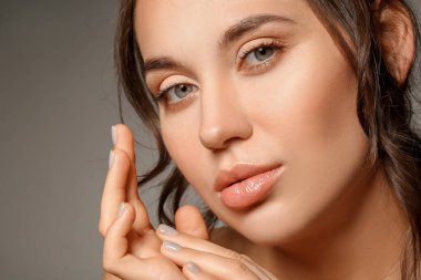 Gri arka planda doğal makyajı olan güzel bir genç kadın. Yakın plan.