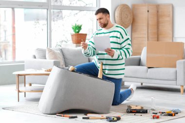 Evdeki koltuğu elle monte eden genç adam.