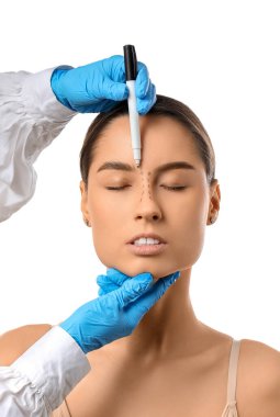 Koruyucu eldivenli doktor beyaz arka planda estetik ameliyat için kadının burnuna izler çiziyor.
