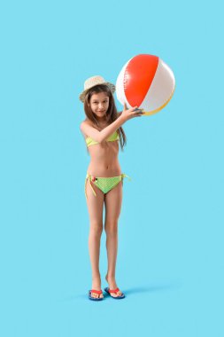 Mavi arka planda plaj topu olan mayolu ve şapkalı şirin küçük kız.