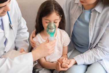 Annesi ve doktoruyla birlikte küçük kız evde nebulizör kullanıyor, yakın plan.