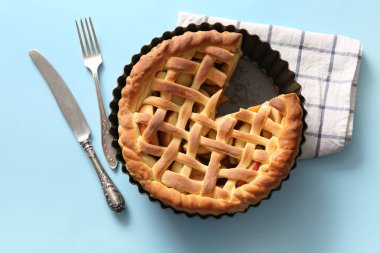 Lezzetli ev yapımı elmalı turta, peçete ve çatal bıçak seti mavi arka planda.