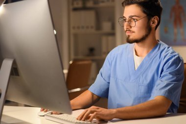 Klinikteki akşam vardiyasında çalışan bilgisayarlı erkek hemşire.