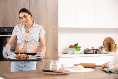 Genç hamile kadın mutfakta kek pişiriyor.