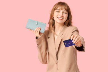 Güzel genç bir kadın pembe arka planda kredi kartı ve cüzdan taşıyor.