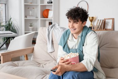 Patlamış mısırlı erkek öğrenci evdeki kanepede televizyon izliyor.
