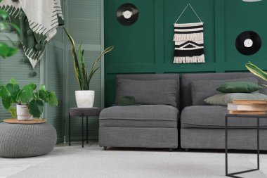 Yeşil oturma odasının içi, rahat siyah kanepesi, sehpası ve çiçekleri olan.