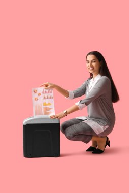 Pembe arka planda kağıt öğütücüyle belgeleri yok eden genç bir kadın.