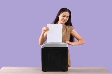 Masadaki kağıt öğütücüsünü kullanarak leylak arka planına zarar veren genç kadın.