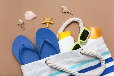 Terlikli çanta, güneş gözlüğü ve kahverengi arka planda güneş kremi şişesi.