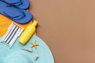 Kumsal aksesuarları ve kahverengi arka planda bir şişe güneş kremi.