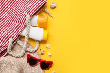 Sarı arka planda güneş kremi şişeleri olan plaj aksesuarları.