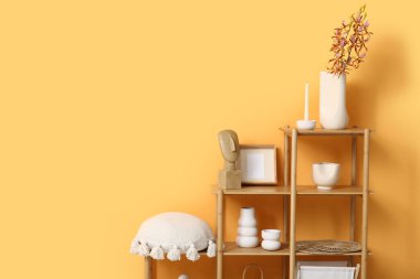 Yastıklı, çerçeveli ahşap raf ünitesi, turuncu duvarın yanındaki vazolar oturma odasında.