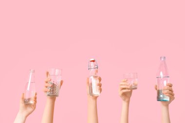 Bardaklı kadın elleri ve pembe arka planda su şişeleri.