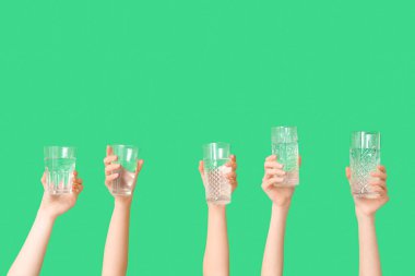 Yeşil arka planda farklı su bardakları olan kadın eller, yakın plan.