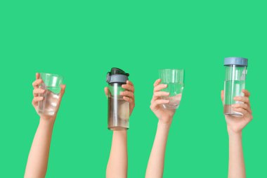 Yeşil arka planda şişe ve bardak su taşıyan kadın eller, yakın plan.