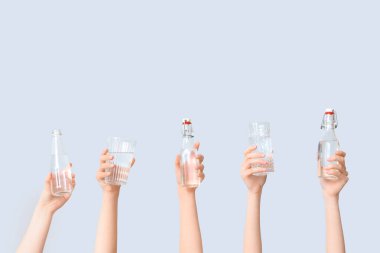 Şişeli kadın elleri ve gri arka planda bir bardak su.