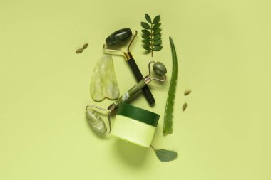 Yüz masajı silindiri, guasha, krema ve bitkiler yeşil arka planda