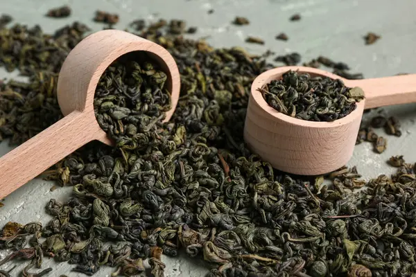 Ahşap kaşıklar, kuru yeşil çay yaprakları ve grunge yeşil arka plan.