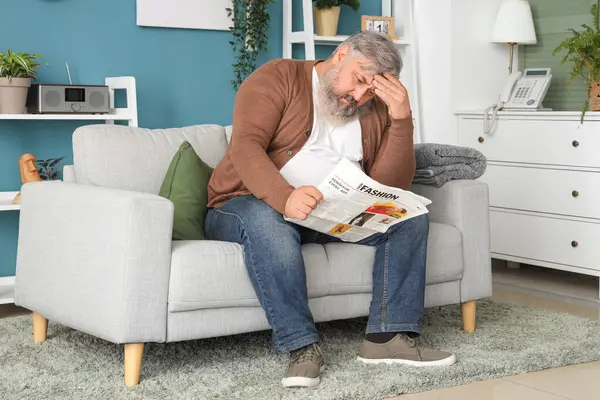 Oturma odasında gazete okuyan üzgün yaşlı adamın portresi.