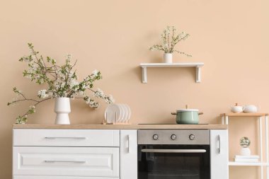 Bej mutfaktaki beyaz tezgahın üzerinde çiçek açan bir vazo.