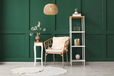 Yeşil oturma odasındaki rahat koltuğun yanındaki sehpanın üzerinde çiçek açan bir vazo.