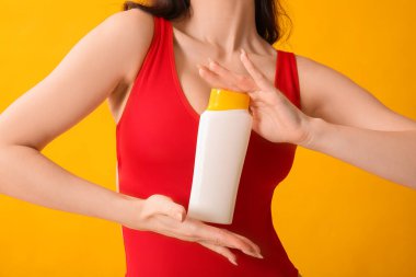 Sarı arka planda güneş kremi şişesi olan genç bir kadın.