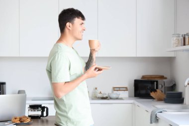 Genç adam mutfakta kahve içiyor.