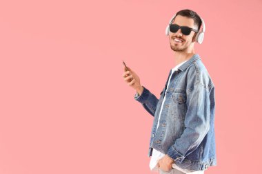 Kulaklıklı, cep telefonlu, pembe arka planda müzik dinleyen genç sakallı adam.