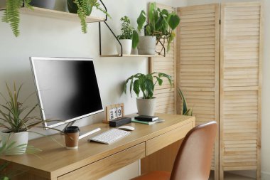 Workplace with computer and green houseplants in light office