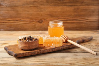 Kitchen board with sweet honey, combs and beebread on wooden background
