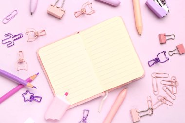 Pembe arka planda farklı kırtasiye malzemesi içeren defter.