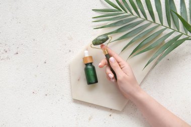 Taş yüz masajlı kadın eli ve hafif arka planda serum.