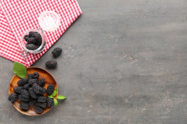 Gri arka planda taze böğürtlenli ahşap tabak ve kavanoz.