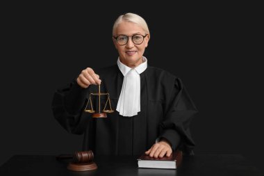 Adalet terazisi ve siyah arka plan kitabı olan olgun bir kadın yargıç.