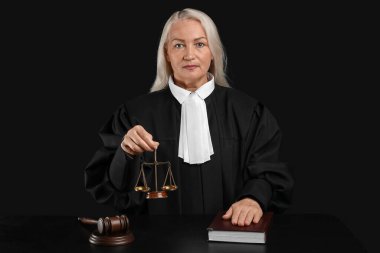 Adalet terazisi ve siyah arka plan kitabı olan olgun bir kadın yargıç.