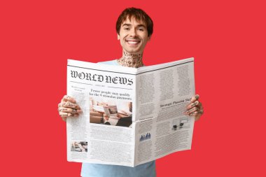 Kırmızı arka planda gazetesi olan yakışıklı bir genç.
